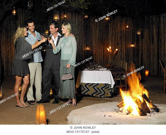 Four people toasting at outdoor nightclub near bonfire night