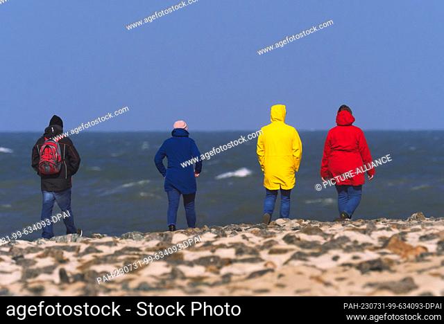 11 April 2023, Lower Saxony, Wangerooge: 11.04.2023, Wangerooge. People in colorful functional clothing walk on the shore of the North Sea on the East Frisian...