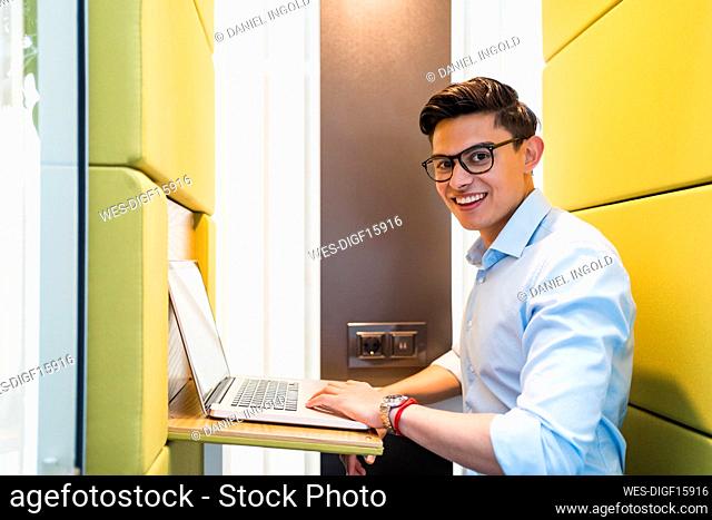 Male professional with laptop smiling while sitting in soundproof booth