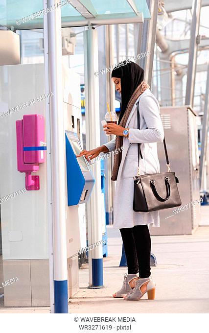Hijab woman using ticket vending machine at railway station