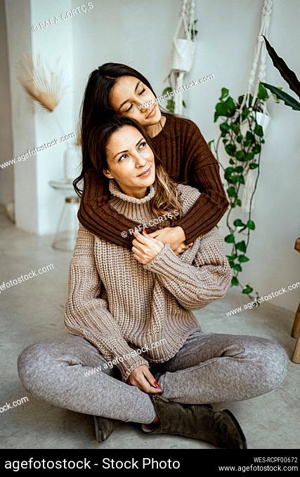 Daughter with eyes closed embracing mother while looking away at home