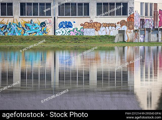 14 December 2023, Baden-Württemberg, Riedlingen: A hall sprayed with graffiti is reflected in the floodwater. The flood situation remains tense in parts of...