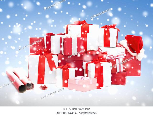 holidays, winter, birthday and celebration concept - christmas presents, decoration paper and santa helper hat over blue background with snow