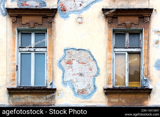 Two old box windows of a yellow house with a damaged facade