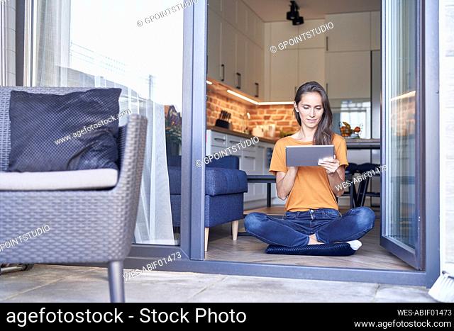 Woman using digital tablet while sitting cross-legged at doorway