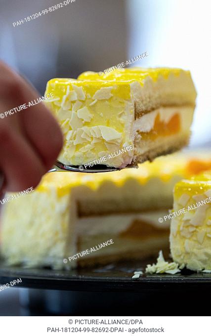 04 December 2018, North Rhine-Westphalia, Mettingen: A person lifts a piece of tangerine mascarpone cake from a plate by the food manufacturer Coppenrath and...
