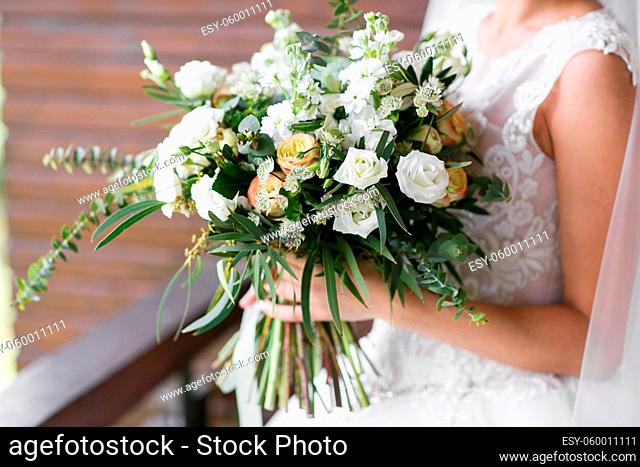 Bridal bouquet. The bride's bouquet. Beautiful bouquet of white flowers and greenery, decorated with silk ribbon, lies on vintage wooden chair