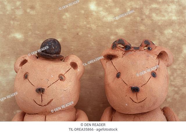 Two small clay model teddy bears standing side by side with one wearing tiny bowler hat and one with hair-ribbon