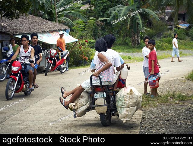 People on motorbikes traveling through rural village outside Calapan City - Philippines
