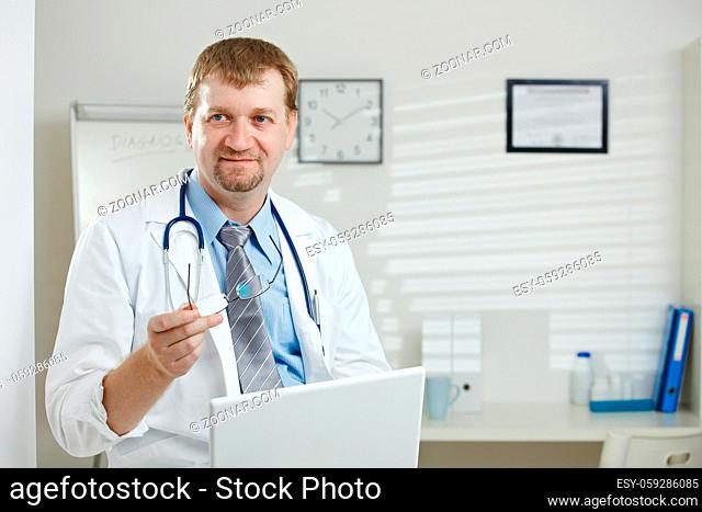 Medical office - male doctor sitting, holding laptop computer in hand, explaining