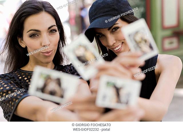 Two happy twin sisters holding instant photos