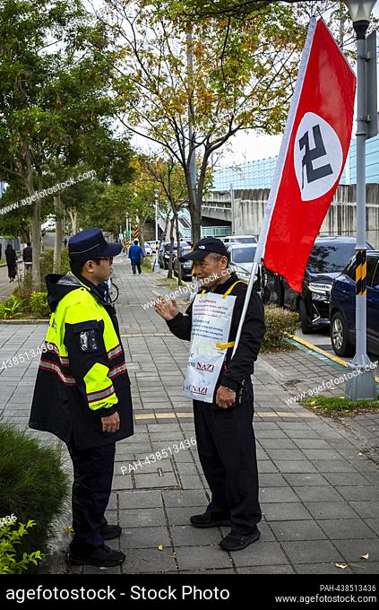 A protester discuss with a police officer when holding a flag emblazoned with the Nazi symbol in front of the European School in Taipei, Taiwan, on 13/12/2023