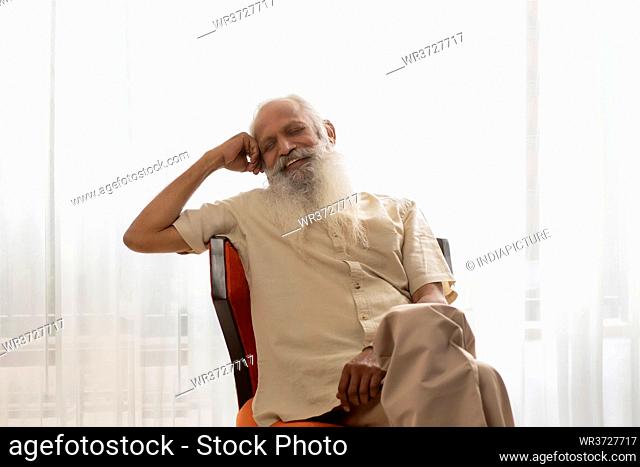 AN OLD MAN SMILING WHILE SITTING AND RESTING ON CHAIR