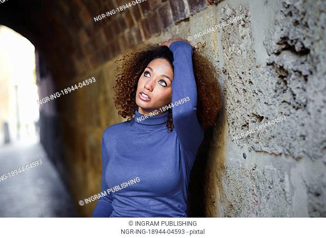 Beautiful young African American woman, model of fashion, with afro hairstyle and green eyes wearing blue sweater in urban background