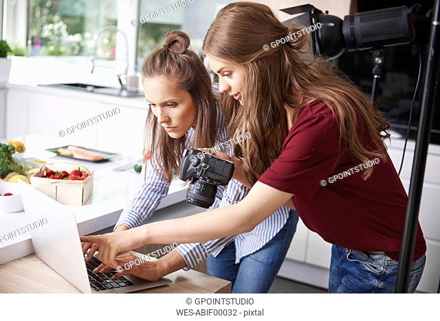 Bloggers using laptop and camera in kitchen