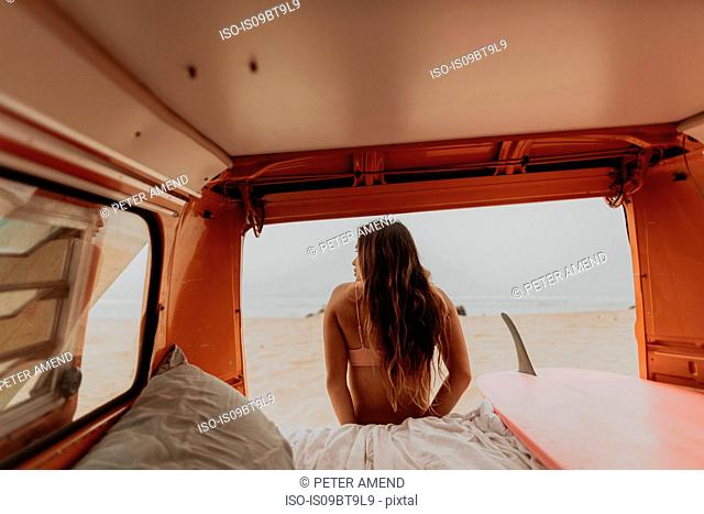 Young female surfer looking out from recreational vehicle, rear view, Jalama, California, USA