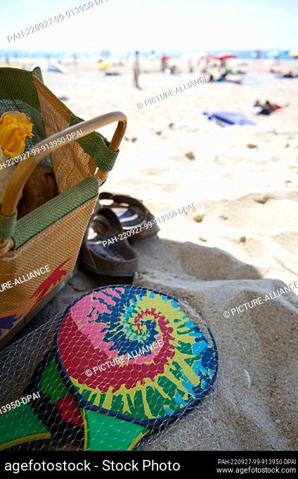 PRODUCTION - 14 August 2022, Portugal, Pataias: A beach ball set and a beach bag are lying in the sand at the beach ""Praia de Vale Furado"" under a parasol
