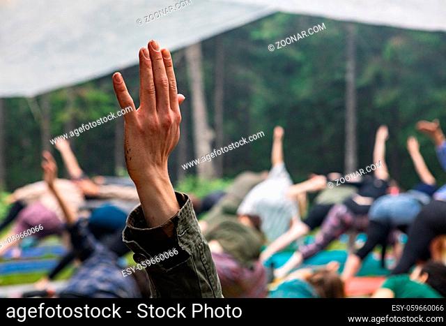 A close up view on the raised hand of a caucasian person during a set of mindful stretching exercises in nature, with blurry people in background and copy space