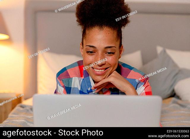 Mixed race woman lying in a bed using a laptop and smiling