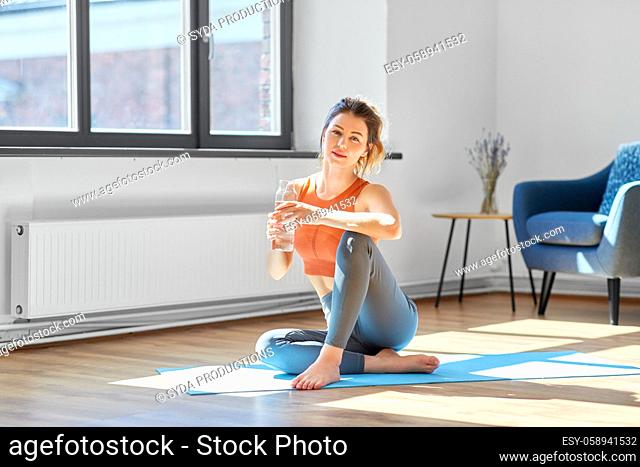 woman with water resting on yoga mat at home