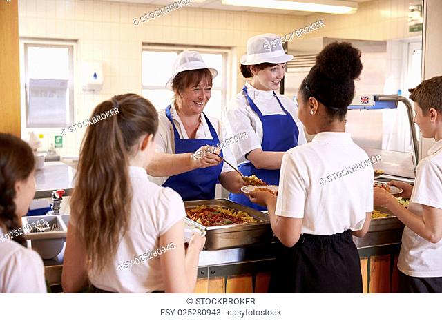 Two women serving kids food in a school cafeteria, back view