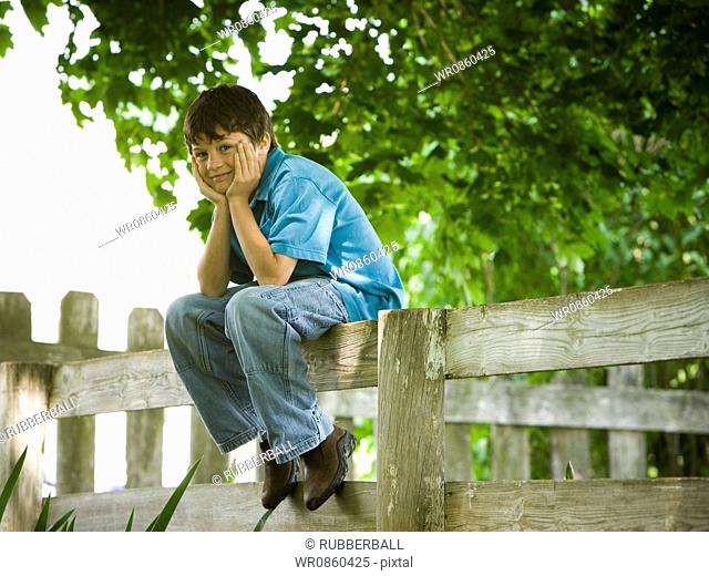 Portrait of a boy sitting on a wooden fence