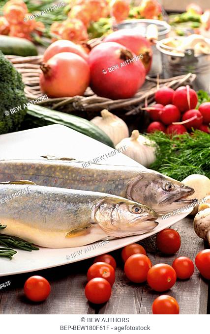 Top view on huge wooden table: two raw, fresh rainbow trouts among vegetables. Idea of healthy living and valuable, natural food