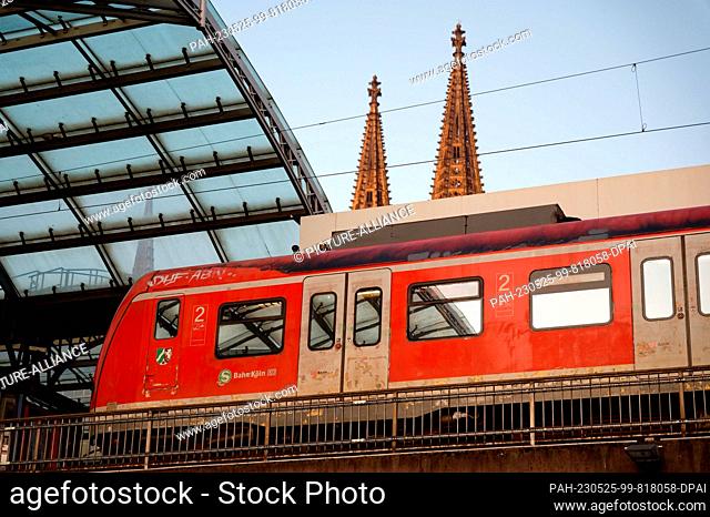 25 May 2023, Hesse, Cologne: A suburban train stands in the main station in Cologne. The spires of the cathedral can be seen in the background