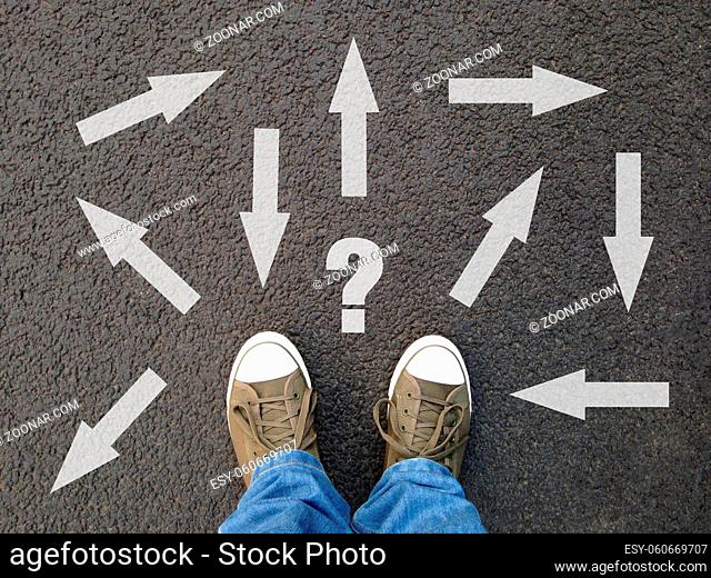 feet standing on asphalt with multitude of arrows in different directions and question mark, confusion choice chaos uncertainty concept