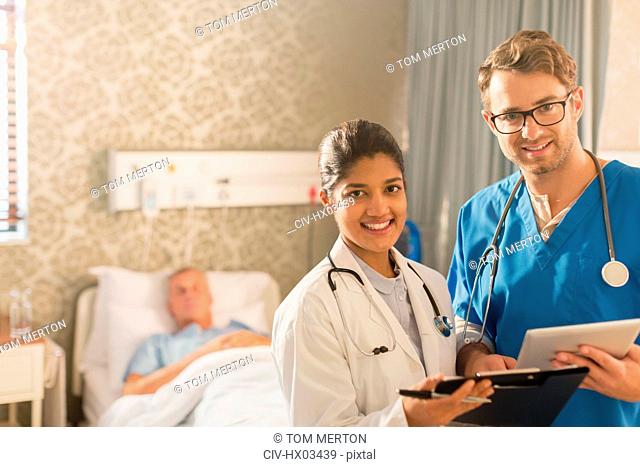 Portrait smiling, confident doctor and nurse making rounds, using digital tablet and clipboard in hospital room