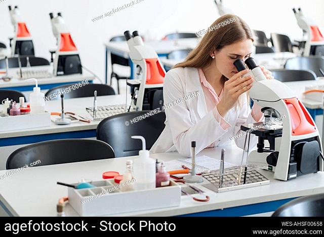 Young researcher in white coat working with microscope in lab