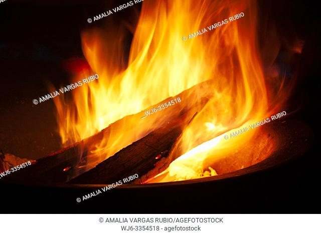 Approaching logs burning between the flames to fan the fire that illuminates a black night