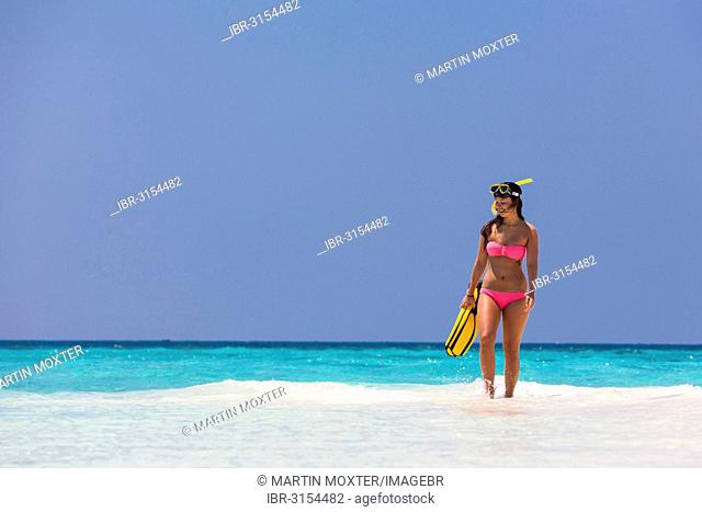 Young woman, about 20, walking over a sandbank with snorkeling gear