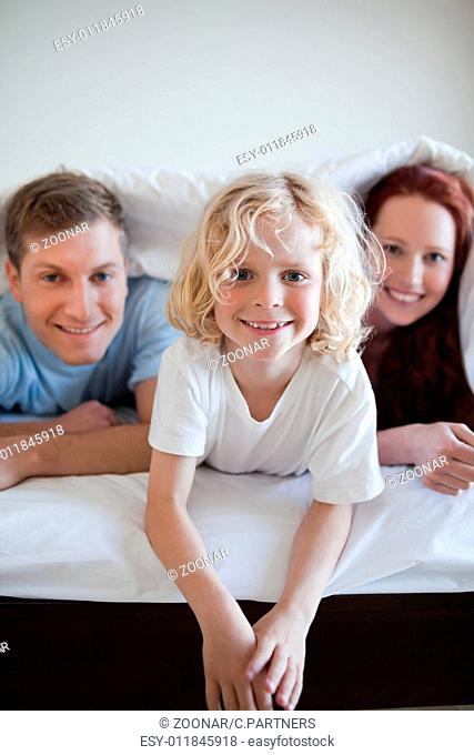 Cheerful boy under the bed cover with his parents