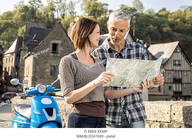 Caucasian couple near blue motor scooter reading map