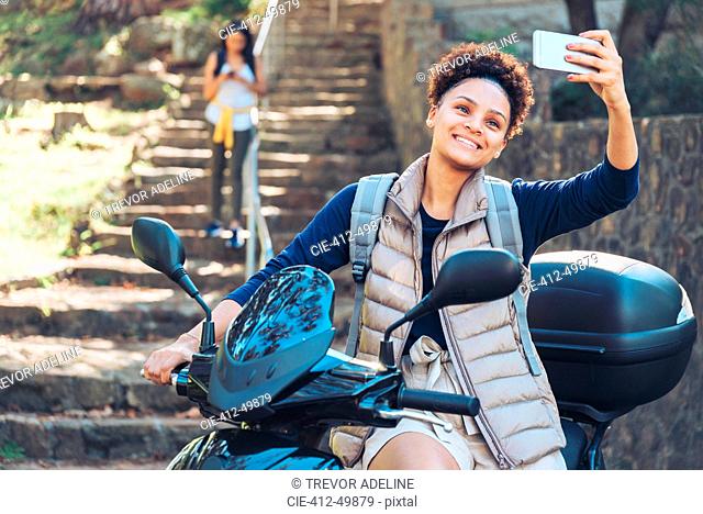 Young woman taking selfie with camera phone on motor scooter