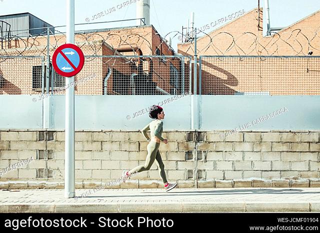 Woman in sports clothing running on footpath by brick wall