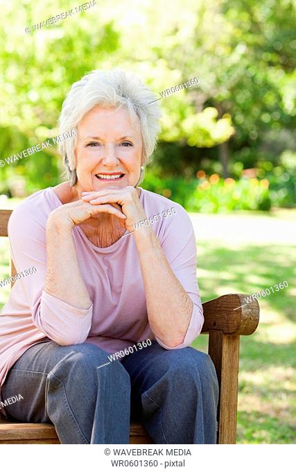 Woman smiling as she rests her head on her hands as she sits on a bench