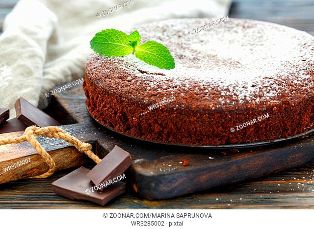 Chocolate cake sprinkled with powdered sugar and mint on old wooden table, selective focus