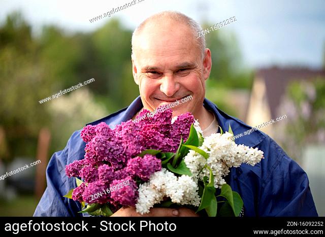 Elderly man with a bouquet of flowers. Brutal gray-haired man with a beautiful lilac