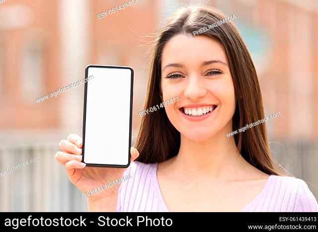 Front view portrait of a happy teen showing smart phone blank screen in the street