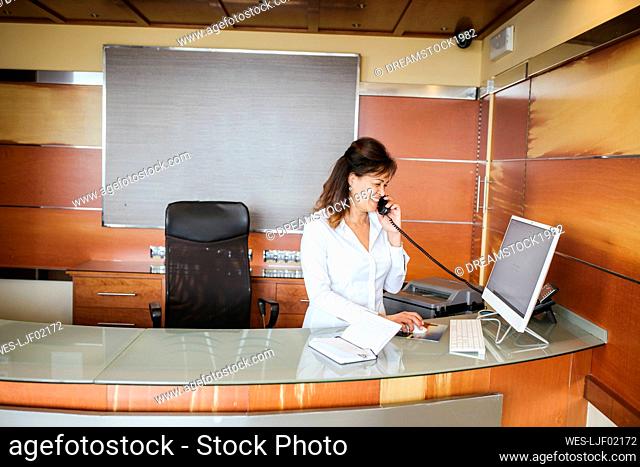 Female receptionist smiling and talking on telephone at reception desk