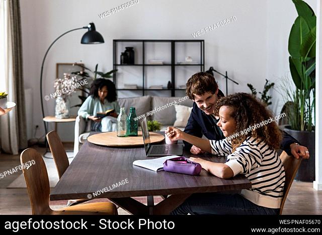 Father watching daughter doing homework with mother reading in background