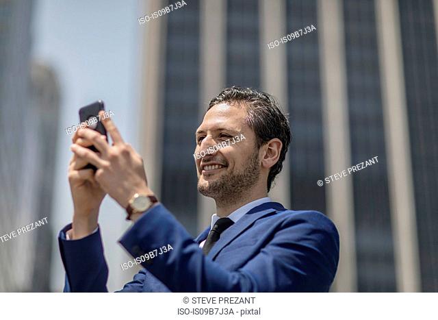 Smiling young businessman taking selfie outside office building, New York, USA