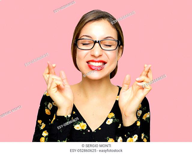 Young woman with glasses crossing her fingers and wishing for good luck with closed eyes, retro vintage style with pink background