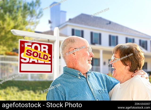 Happy Affectionate Senior Couple Hugging in Front of Sold Real Estate Sign and House