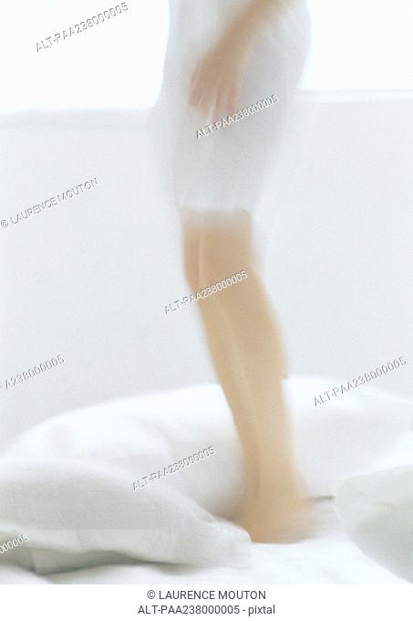 Woman standing on bed, low section, blurred