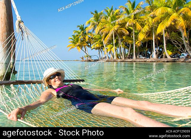 Woman enjoys hammock in tropical waters and Palapa platforms, North Long Coco Plum Caye, Belize