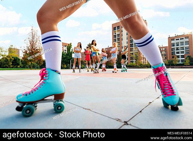 Friends wearing roller skates at sports court seen through woman's leg