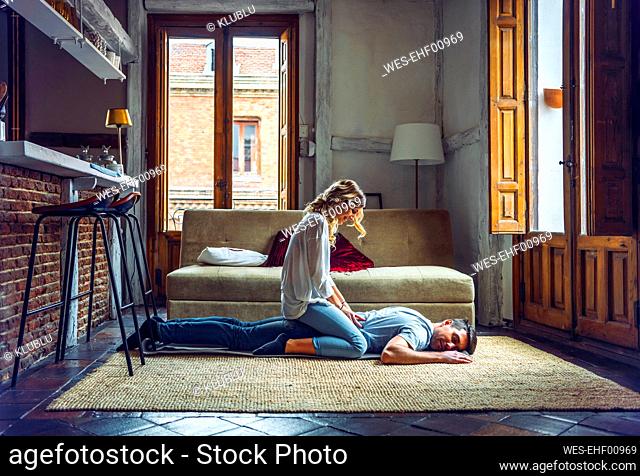 Young woman massaging boyfriend lying on rug in living room at home